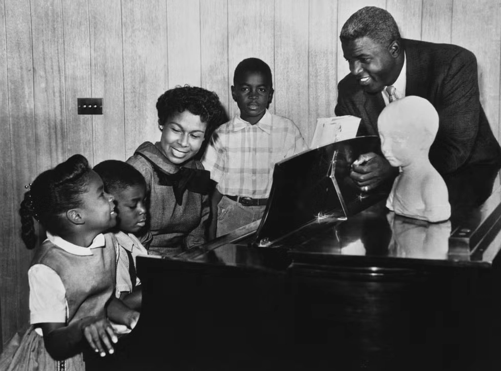 Một người phụ nữ ngồi chơi piano với hai đứa trẻ, một người đàn ông và một đứa trẻ khác đứng phía sau nhạc cụ, Tiểu sử Jackie Robinson