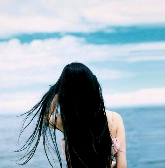 Cô gái tóc dài quay lưng đứng lặng lẽ trước sóng biển rì rào