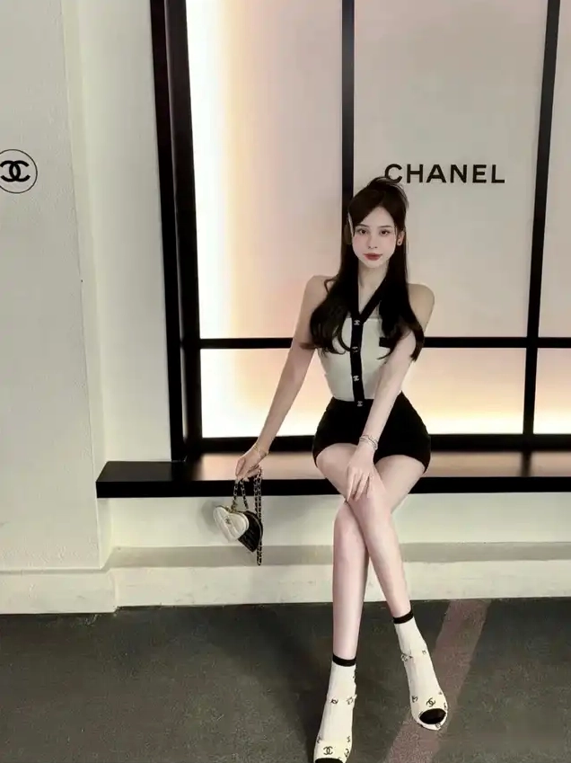 Cô gái trẻ xinh đẹp ngồi tạo dáng với túi xách hình trái tim trước phông nền Chanel sang trọng