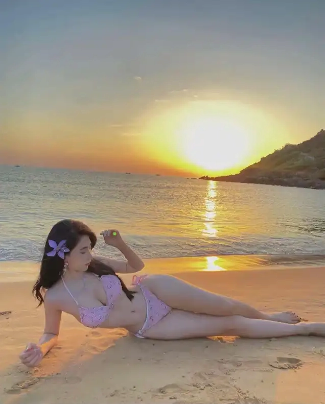 Mỹ nữ mặc bikini màu hồng nằm nghiêng trên bãi cát ngắm hoàng hôn rực rỡ