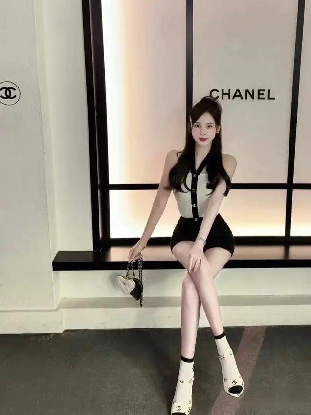 Người đẹp mặc đồ tông đen trắng cầm túi hình trái tim ngồi trước background Chanel
