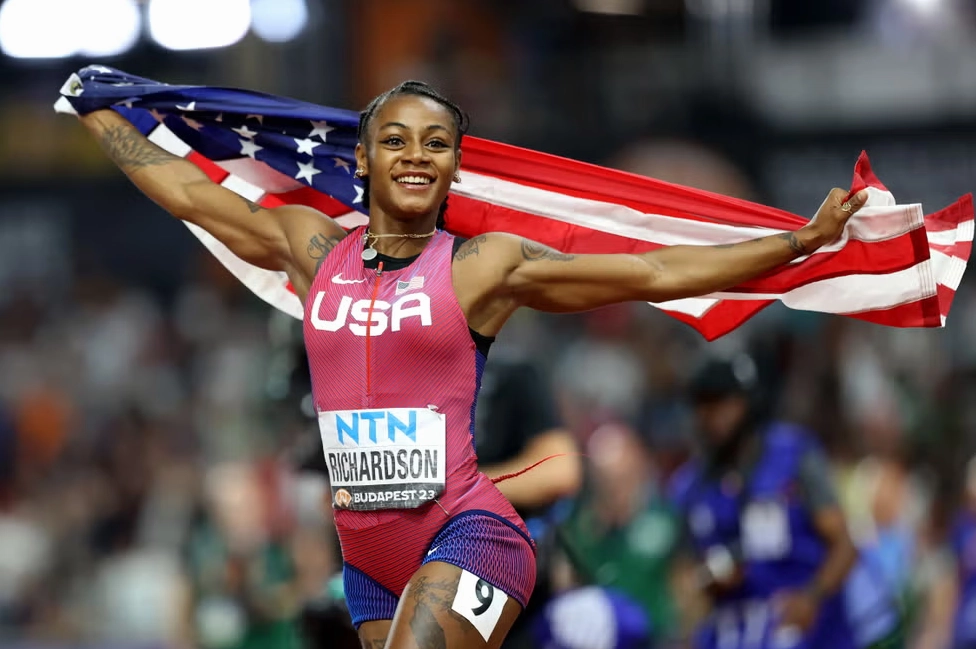 Sha Carri Richardson rạng rỡ ăn mừng chiến thắng với lá cờ Mỹ tung bay phía sau